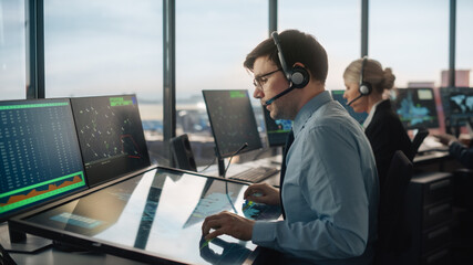 Male Air Traffic Controller with Headset Talk on a Call in Airport Tower. Office Room is Full of...