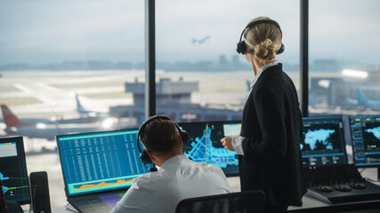 Female and Male Air Traffic Controllers with Headsets Talk in Airport Tower. Office Room is Full of Desktop Computer Displays with Navigation Screens, Airplane Departure and Arrival Data for the Team. © Gorodenkoff