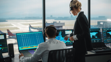 Female and Male Air Traffic Controllers with Headsets Talk in Airport Tower. Office Room is Full of Desktop Computer Displays with Navigation Screens, Airplane Departure and Arrival Data for the Team. - obrazy, fototapety, plakaty