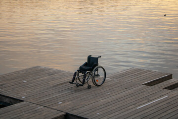 Empty wheelchair on wooden bridge. Wheelchair parked by water. 