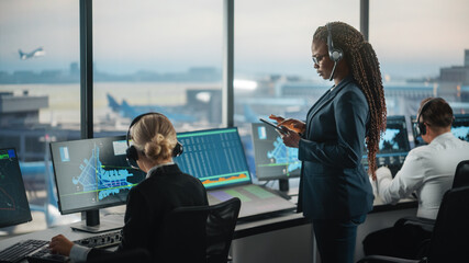 Black Female Air Traffic Controller Holding Tablet in Airport Tower. Office Room is Full of Desktop...