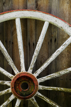 old white wooden carriage wheel and spokes besides a wooden building
