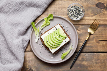 Rye bread toast with goat cheese and avocado on wooden table background. Healthy avocado open...