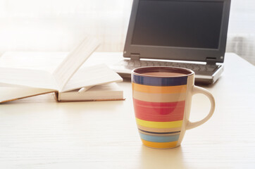Workplace at a table near a bright window, a coffee mug on a blurry background of a notebook and laptop