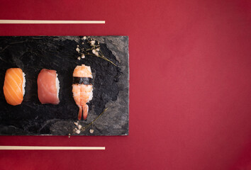 Three nigiri sushi on a black plate with two small flowers on the sides and copy space on the right side.