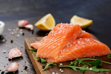 Raw fillet of salmon with sea salt, lemon and pepper on black stone background.
