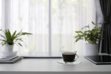 Black tea in glass cup on and black tablet with plants pot on white desk