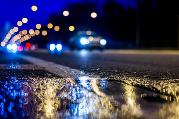 Night city lights reflected in a puddle, light from the headlights of approaching cars. Close up...