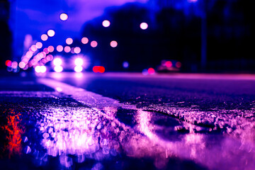 Night city lights reflected in a puddle, light from the headlights of approaching cars. Close up...