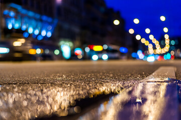 Nights lights of the big city, the night avenue with cracked asphalt and headlights of the driving cars. Close up view from the level of the dividing line