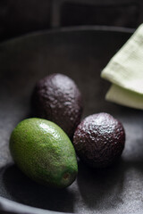 Green and brown avocados in a dark pan with a napkin. Back light. Vertical shot