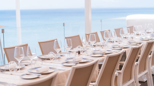 Mesa de restaurante preparada para servicio en boda con vistas al mar en terraza. Imagen agradable y fresca hosteler&iacute;a.