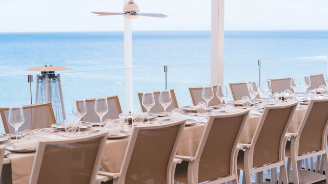 Mesa de restaurante preparada para servicio en boda con vistas al mar en terraza. Imagen agradable y fresca hosteler&iacute;a.