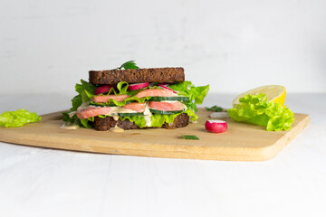 sandwich with salmon and vegetables on brown bread on wooden board on white background