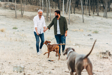 happy gay male couple walking with their dogs in the countryside. lgbt guys playing with their dogs outside.