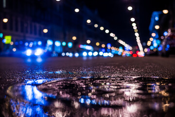 Fototapeta na wymiar Nights lights of the big city, the main city street in rushhour. Close up view of a puddle on the level of the hatch