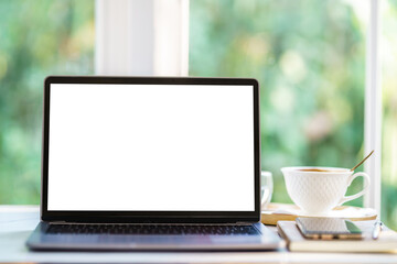Fototapeta premium Mockup of laptop computer with empty screen with notebook,coffee cup and smartphone on table side the window in the coffee shop at the cafe,White screen
