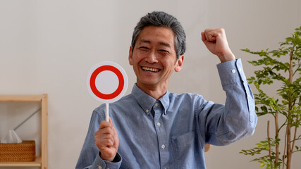 笑顔でまるのプレートを持つシニア男性