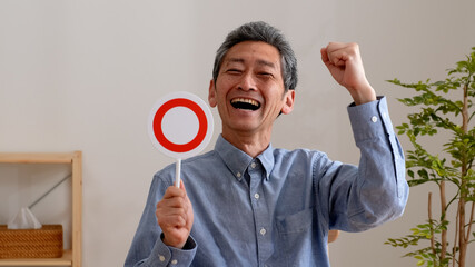 笑顔でまるのプレートを持つシニア男性