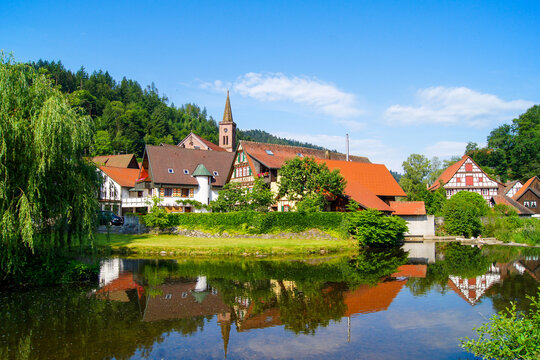 Scenic view of the small medieval village of Schiltach, Germany with its church tower in the center. Beautiful half-timbered houses and weeping willow reflect in the river's water.