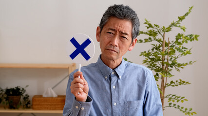 悲しい表情でバツのプレートを持つシニア男性