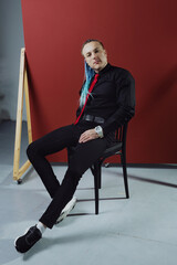 Young attractive man with an interesting haircut in braids on an undercut with a red tie on a red background