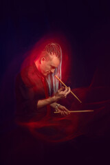 Handsome man with interesting braids on a black background with drumsticks, shot with mixed light