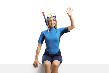Woman in a wetsuit and a diving mask sitting on a banner and waving