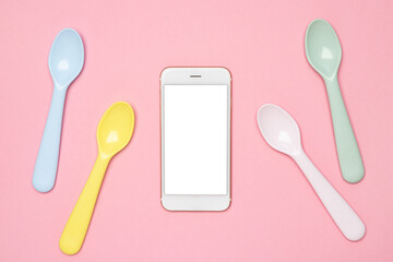 Mobile phone mock up nd Kid spoons in different colors laid on sweet pink pastel background, a set...