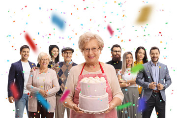 Grandmother with a cake and people gathered behind with confetti in the air at a celebration
