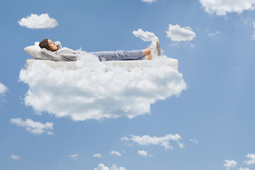 Teenage girl in jeans and hoodie resting on a mattress on clouds