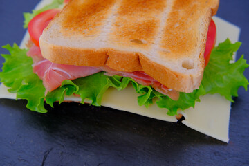 close-up of an appetizing sandwich with ripe tomato slices, green salad, cheese, ham, browned toasted toast, quick snack concept, fast food cooking at home, chef preparing a sandwich