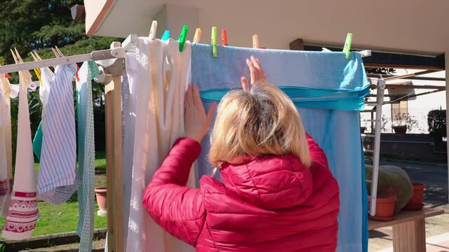 Blonde housewife hanging up clean laundry outdoors on dryer, busy female washing dirty linen and drying on fresh air. Concept of housekeeping and hygiene