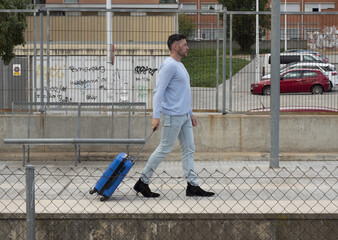 a 40 to 45 year old man walks with a blue suitcase, at the exit of a station.