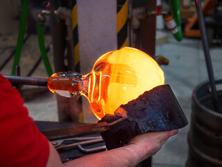 Artistic glassmaker shapes molten glass with wooden tool.