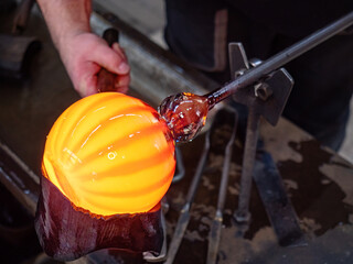 Glassblowing crafter rounds the hot-striped vase  with wet woode tool