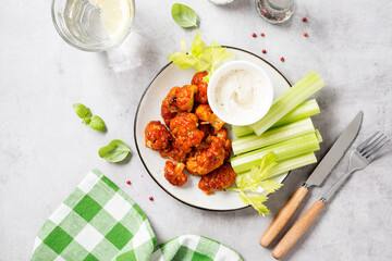 Buffalo style barbecue cauliflower  with fresh celery sticks  and sauce . Light gray stone...