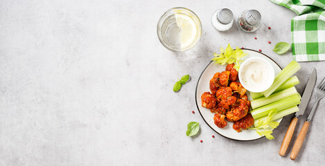  Buffalo style barbecue cauliflower  with fresh celery sticks  and sauce . Light gray stone background. Top view. Space for text