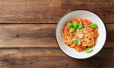 Tasty appetizing classic italian spaghetti pasta with tomato sauce,  parmesan cheese and fresh basil leaves. Wooden background, top view