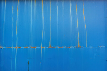 Fragment of a blue metal wall. There is a joint of two sheets with splits of welding and rusty streaks on the surface. Background. Texture.