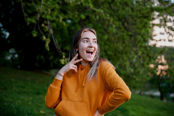 A young European happy woman wearing orange hoodie looking to the right. The model is showing a peace sign. A fun picture with a model showing a kiss. Bright colourful fun photo. Copy space for text.