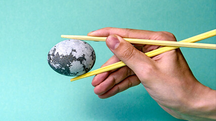 A space egg in the hands of a young man with Japanese chopsticks on a neon background. Minimal Easter holiday or food concept. Abstract concept of egg painting.
