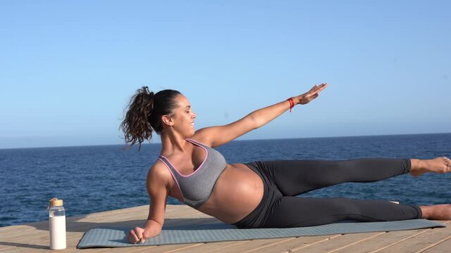 Young hispanic pregnant woman doing sport exercise outdoor on the beach - Healhty lifestyle and life balance concpet