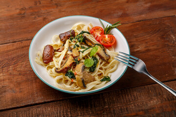 Udon with mushrooms and spinach and cherry tomatoes in a plate on a wooden table next to a fork.