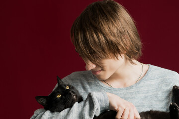 A young guy with long hair holds a cat in his hands