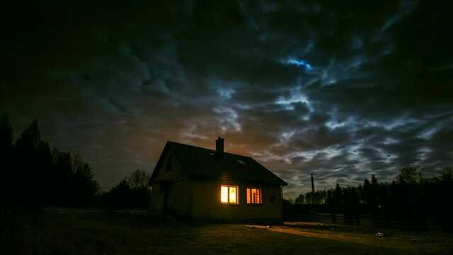 Time lapse with small house in night forest under cloudy sky with moon. 