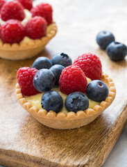 Homemade tartlets with custard, raspberries and blueberries on the wooden table, close up