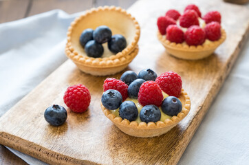 Homemade custard tartlets with raspberries and blueberries on the wooden table, close up