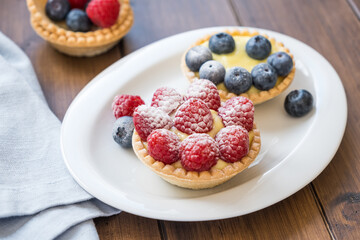 Homemade tartlets with custard, raspberries and blueberries on the white plate, close up