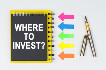 On a white background lies a pen, arrows and a notebook with the inscription - WHERE TO INVEST